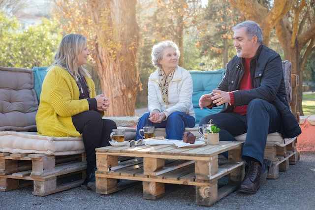 three seniors sitting outside on lawn furniture talking